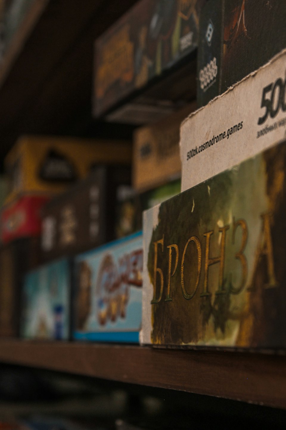 Several board game boxes are stacked on a wooden shelf.