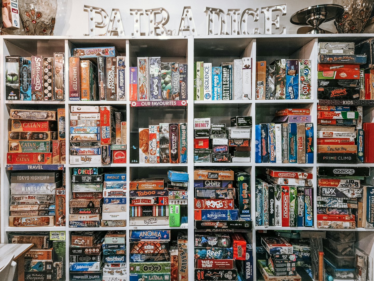 Hundreds of board games organized on white shelves with 'PATRA DICE' sign.